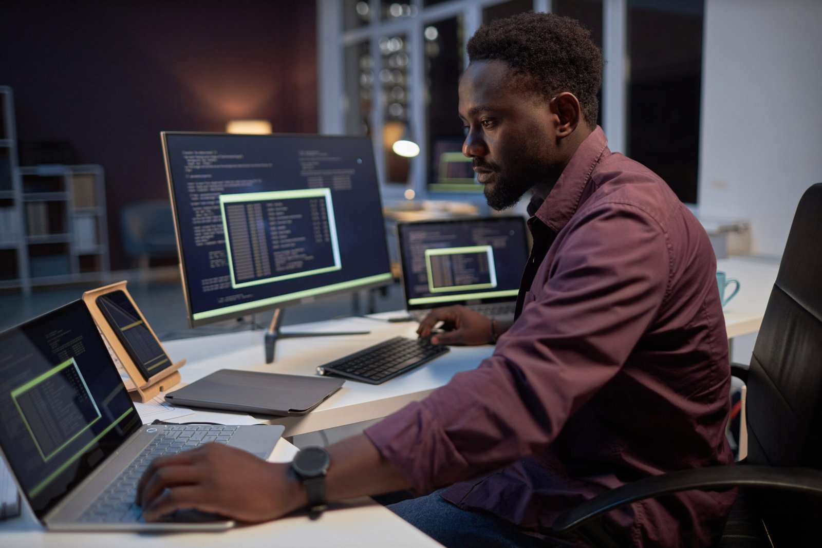 African American programmer concentrating on his online work on computers while working in office till late evening